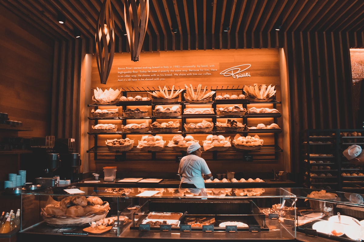 Interior de panadería con estantes de pan y panadera trabajando